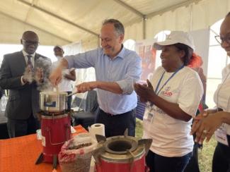 U.S. Second Gentleman stands in the middle of the photo, stirring a metal pot. On either side of him, there are people smiling and clapping. 