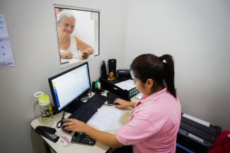 Woman works a on computer assisting another woman who is standing in front of her.