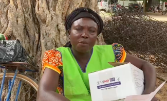 A woman sits next to a tree with a box of antimalarial medicines