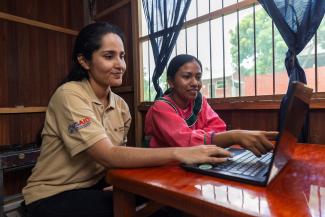 An extenionist woman and an indigenous young woman sitting in front of a computer