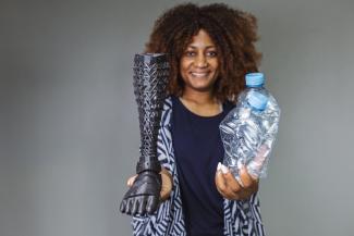 Martela Vania Uetela stands holding a prosthetic in one hand and plastic water bottles in another.