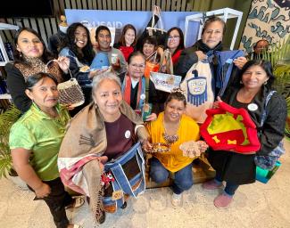 A group of entrepeneur women with a USAID officer smiling and showing their products made with recycled plastic