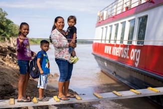 Indigenous woman with her children walking on top of a plank, going onboard an hospital ship.