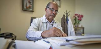 A doctor sits behind a desk working on patient charts