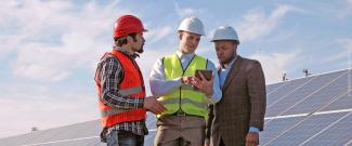 Three engineers examine data on a tablet in front of a large photovoltaic array