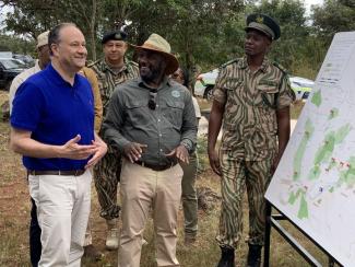 U.S. Second Gentleman Douglas Emhoff stands in a group while viewing a map of Zambia that is shaded to represent the location of the country's national parks.