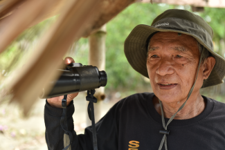 A man in a hat holds a pair of binoculars. 