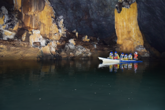 A boat with several people in lifejackets and helmets floats through an underground river