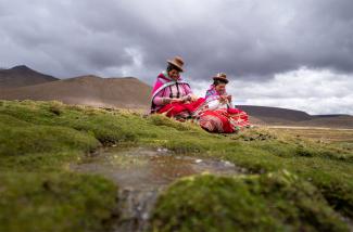 Andean women sitting next to a water stream in the mountains