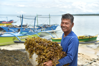 A man smiles holding a basket full of seagrasses