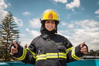 A women in firefighting gear smiles with two thumbs up