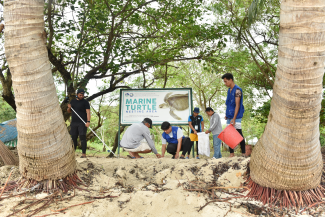 A group of people stand in front of a sign for a turtle protected area. 