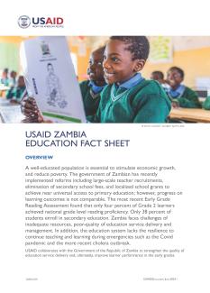 A primary-school age Zambian boy smiles as he reads from a book in the classroom