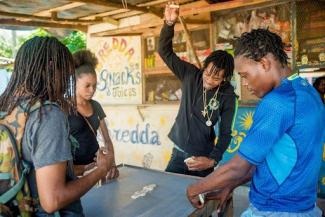 Four young people playing a game of dominos in front of a snack bar.