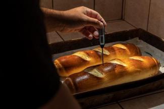 A hand holding a termometer checking the temperature of the bread in the oven