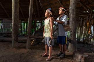 An indigenous old man standing with his hands on the shoulder of a young indigenous boy