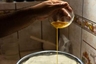 A hand holding a flask and dropping honey into the bread dough