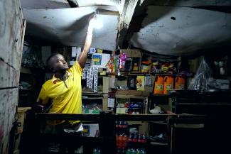 A shopkeeper lights his lamp to illuminate his shop utilizing mobile solar batteries. Kalaf Village, Djibouti.