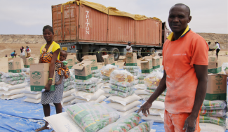 A man and a woman stand amongst humanitarian supplies