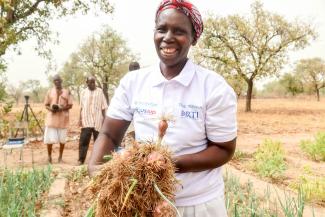 Djenabou Koné, Benkadi cooperative member in Signé village, Koutiala region, proudly displaying the new shallots in her shallot bed. Photo credit: Feed the Future Mali Sene Yiriwa - South