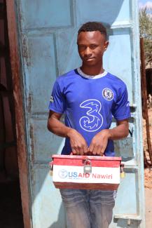 James Lordo proudly carries a VSLA Savings box, belonging to Nakuton Youth group, outside his retail shop. Photo credit: Saruni Letiwa/USAID