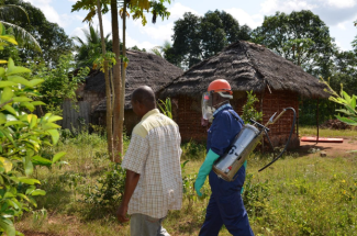 A spray operator is accompanied to a structure in Zanzibar (2017) to spray it with insecticide.