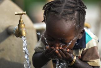 A young girl takes a drink of water from a newly constructed water tank. In 2017, USAID provided clean drinking water for more than 300,000 people in Ethiopia. Photo credit: AECOM.