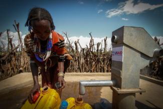 A woman in Buluko fills her containers from a water pump that USAID helped construct. Photo credit: AECOM.