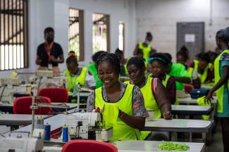 Rows of women wearing yellow vests seated behind sewing machines