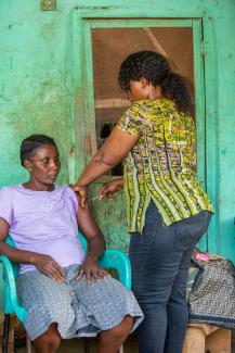 A nurse standing over a seated woman injecting contraceptive.