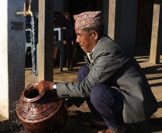 Jogiram Buda Chhetri fills a water container outside his house in Bijulekh village. Jogiram normally migrates to a nearby city during the dry season since his village had no water for part of the year. Now the village has a new solar-lift water supply and sanitation (WSS) systema and homes have a water tap, supported by the USAID Karnali Water Activity and managed by the Water Users and Sanitation Committee. 