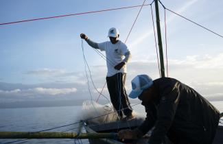 Two men adjust nets and lines on a fishing boat