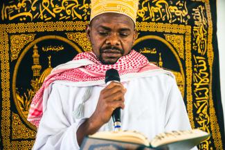 A man reading from a book while holding a microphone.