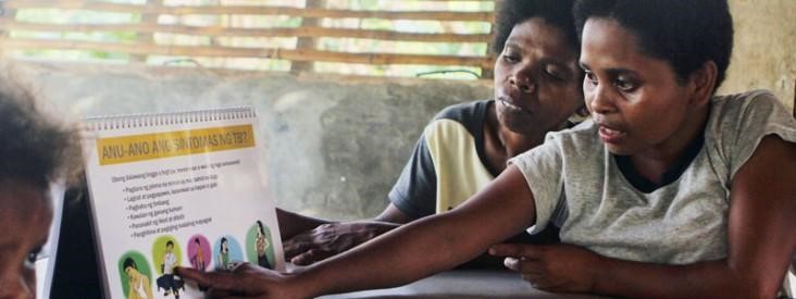 Women look through a flipchart that helps debunk TB myths.