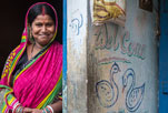 A woman leans against a wall and smiles at the camera. 