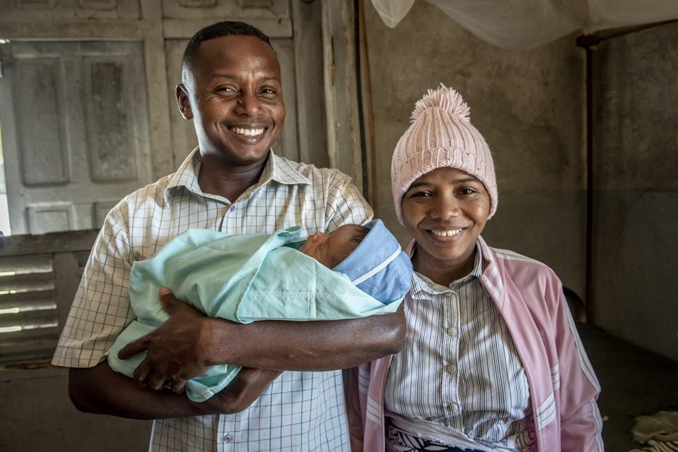 Parents smile for the camera, the father holding an infant